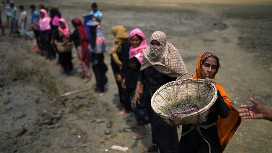 Rohingya refugee women carry baskets of dried out mud from the riverbed to help raise the ground level of the camp in preparation for monsoon season, in Shamlapur refugee camp in Cox's Bazaar, Bangladesh, March 24, 2018.  Credit: Clodagh Kilcoyne/Reuters