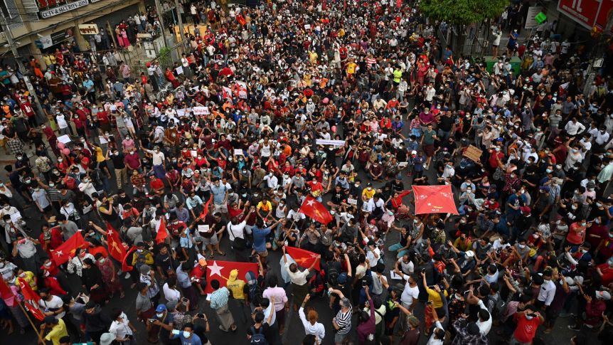 Protesters carry red flags and wear red headbands to show support for Aung San Suu Kyi's National League for Democracy party. (AFP: Ye Aung Thu)