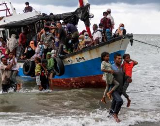 Locals evacuate Rohingya refugees from a boat that came ashore on the north coast of Indonesia's Sumatra island in June 2020. The UNHCR says the journey across the Andaman Sea last year was deadlier than ever before [Rahmad/Antara Foto via Reuters]
